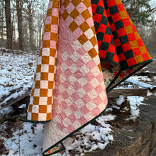 Load image into Gallery viewer, Checkered quilt with orange, black, and pink pattern on a gravel path with trees in the background. Norma Jean bundle available at globalfibershop.com.