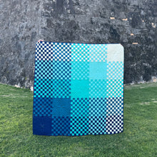 Load image into Gallery viewer, Blue and white checkered mat on grass with a stone wall background