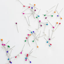 Load image into Gallery viewer, Scattered assortment of rainbow pearl glass-head pins from Rico Design sold at Global Fiber Shop.