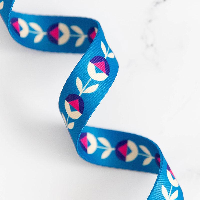 Blue ribbon with floral pattern on a white background. Bags, totes, key rings - the possibilities are endless! We are now stocking fun and flirty webbing, designed by your favorite Ruby Star Society designers for Stitch Supply Co. Available at globalfibershop.com.