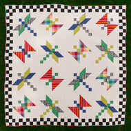 Colorful quilt with geometric pattern on a checkered border. Dragonfly Lake Quilt in Picnic Wovens by Suzy Quits for Art Gallery Fabrics. Available at globalfibershop.com