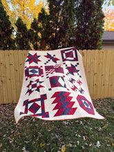 Load image into Gallery viewer, Quilt with red and blue geometric patterns draped over a wooden structure outdoors.
