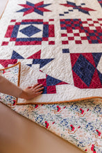 Load image into Gallery viewer, Quilt with red, white, and blue geometric patterns on a wooden surface.
