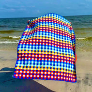 Colorful checkered towel on a sandy beach with ocean waves in the background