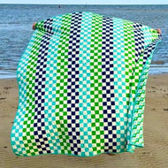 Green and black checkered quilt on a sandy beach with ocean in the background