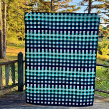 Load image into Gallery viewer, Checkered blanket with blue and green pattern on a wooden deck with trees in the background
