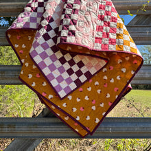 Load image into Gallery viewer, Quilt with checkered and patterned sections draped over a metal railing outdoors.
