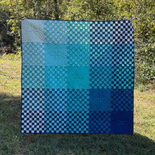 Load image into Gallery viewer, Blue and white checkered quilt on a grassy outdoor area with trees in the background
