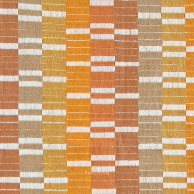 Textile pattern with orange, brown, and white stripes on a grid background. Embrace the charm of the rainbow with Fableism Supply Co’s ‘Lucky Loom’ fabric collection—a dazzling fusion of mixed weight wovens inspired by moments of serendipity. This collection’s palette radiates warmth and whimsy, featuring golden yellows, soft pinks, earthy greens, tranquil blues, and rich purples, each reminiscent of the colors in a lucky rainbow. Available at globalfibershop.com.