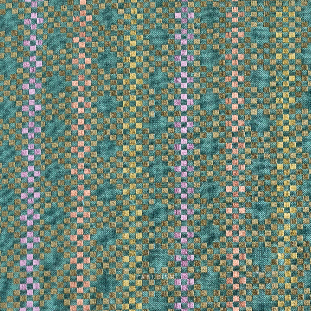 Woven fabric pattern with green, pink, and brown colors. Embrace the charm of the rainbow with Fableism Supply Co’s ‘Lucky Loom’ fabric collection—a dazzling fusion of mixed weight wovens inspired by moments of serendipity. This collection’s palette radiates warmth and whimsy, featuring golden yellows, soft pinks, earthy greens, tranquil blues, and rich purples, each reminiscent of the colors in a lucky rainbow. Available at globalfibershop.com.