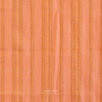 Woven fabric with vertical yellow stitching on a peach background.  Embrace the charm of the rainbow with Fableism Supply Co’s ‘Lucky Loom’ fabric collection—a dazzling fusion of mixed weight wovens inspired by moments of serendipity. This collection’s palette radiates warmth and whimsy, featuring golden yellows, soft pinks, earthy greens, tranquil blues, and rich purples, each reminiscent of the colors in a lucky rainbow. Available at globalfibershop.com.