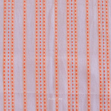 Load image into Gallery viewer, Woven Fabric with orange vertical stripes on a light lavender background.  Embrace the charm of the rainbow with Fableism Supply Co’s ‘Lucky Loom’ fabric collection—a dazzling fusion of mixed weight wovens inspired by moments of serendipity. This collection’s palette radiates warmth and whimsy, featuring golden yellows, soft pinks, earthy greens, tranquil blues, and rich purples, each reminiscent of the colors in a lucky rainbow. Available at globalfibershop.com.
