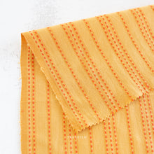 Load image into Gallery viewer, Close-up of yellow fabric with red stitching.  Embrace the charm of the rainbow with Fableism Supply Co’s ‘Lucky Loom’ fabric collection—a dazzling fusion of mixed weight wovens inspired by moments of serendipity. This collection’s palette radiates warmth and whimsy, featuring golden yellows, soft pinks, earthy greens, tranquil blues, and rich purples, each reminiscent of the colors in a lucky rainbow. Available at globalfibershop.com.
