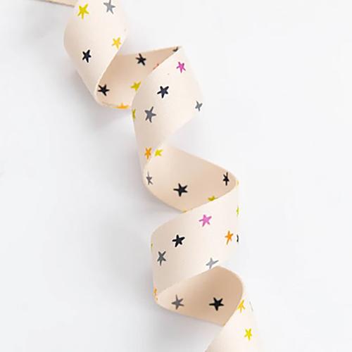 Beige ribbon with colorful star pattern on a white background. We are now stocking fun and flirty webbing, designed by your favorite Ruby Star Society designers for Stitch Supply Co. Available at globalfibershop.com.