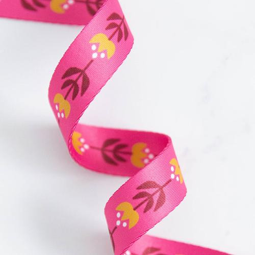 Pink ribbon with floral pattern on a white background. Bags, totes, key rings - the possibilities are endless! We are now stocking fun and flirty webbing, designed by your favorite Ruby Star Society designers for Stitch Supply Co. Available at globalfibershop.com.