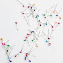 Load image into Gallery viewer, Scattered assortment of rainbow pearl glass-head pins from Rico Design sold at Global Fiber Shop.
